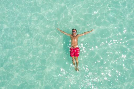 Aerial shot of young man lying down on tropical water floating on his back in Mexico