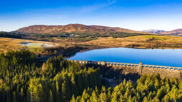A panoramic aerial view, captured by a drone, of a  fresh water reservoir created by building a dam across a Scottish river. The dam was part of the Galloway hydro electric scheme which was built between 1930 and 1936. The loch is in part of the country popular for walking and mountain biking.
The panorama was created by merge several images together.