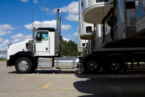 A long haul semi-tractor with a sleeper cab hauling a white aluminum van trailer down an asphalt highway. These types of truck trailer combinations are used for long haul commerce where the truck driver can sleep in the back of their rigs.