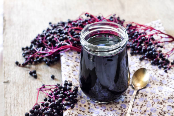 Homemade black elderberry syrup in glass jar Homemade black elderberry syrup in glass jar and bunches of black elderberry in background elderberry photos stock pictures, royalty-free photos & images