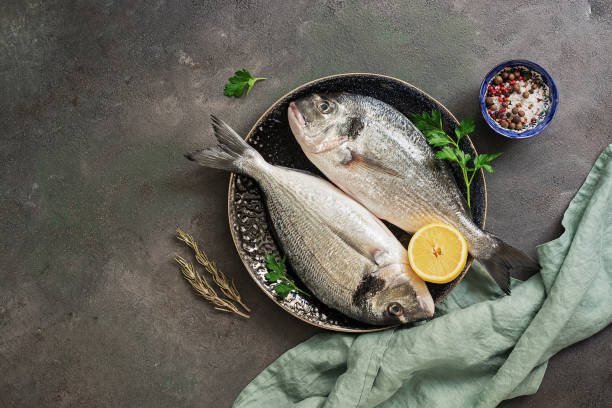 Fresh raw dorado fish in a plate with lemon and parsley on a dark painted background. Top view, flat lay. Fresh raw dorado fish in a plate with lemon and parsley on a dark painted background. Top view, flat lay catch of fish stock pictures, royalty-free photos & images