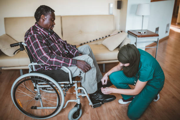 healthcare worker tie shoe laces of disabled senior man. arabian healthcare female worker is helping her disabled afro-american patient - wheelchair disabled senior adult female nurse imagens e fotografias de stock