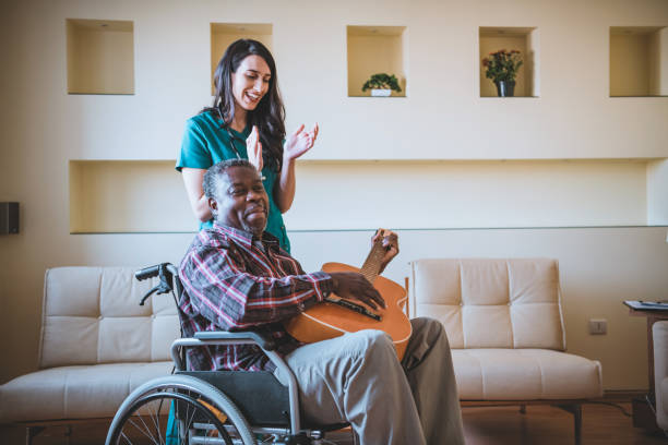 afro-american man in wheelchairs is playing guitar for a female doctor at home - nurse ethnic doctor real people - fotografias e filmes do acervo