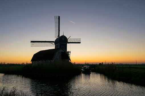 Traditional windmill along a waterside in Holland at dusk.