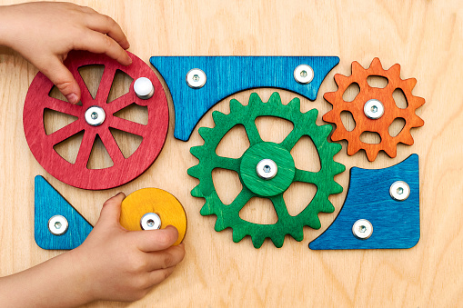 The child rotates toy wooden multi-colored bright gears with two hands. The solution of elementary children's tasks, a complex mechanism