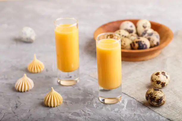 Sweet egg liqueur in glass with quail eggs and meringues on a gray concrete background. Side view, close up.