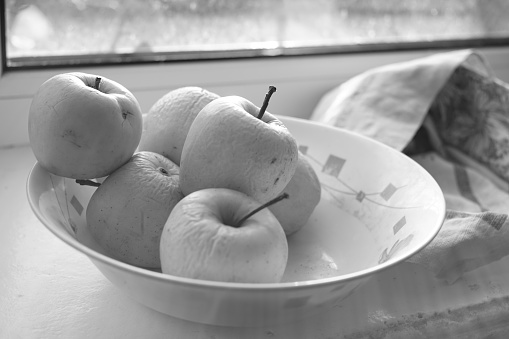 Natural apples in a plate on a windowsill, organic fruits on a sunny winter day