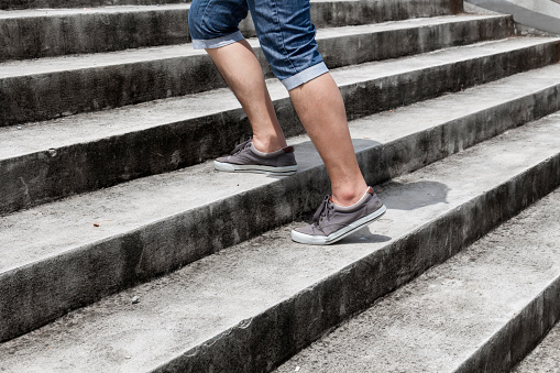 Young man in blue jeans and sneaker shoes walking up stairs outdoors background with copy space for text. Concept of person's lifestyle.