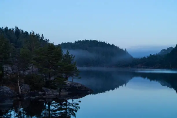 Photo of Still lake with fog, trees and sky.