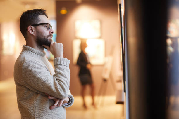 Bearded Man Looking at Paintings in Art Gallery Side view portrait of mature bearded man looking at paintings while enjoying exhibition in modern gallery or museum, copy space museum stock pictures, royalty-free photos & images