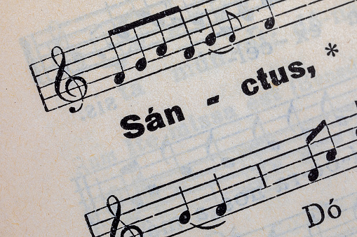 printed word sanctus on the page of an ancient hymnal with staves and musical notes
