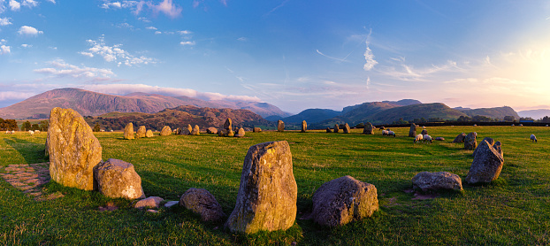 A panorama of the whole stone circle in the summer the circle and the mountains in the background illuminated by the setting sun, sheep grazing between the stones.