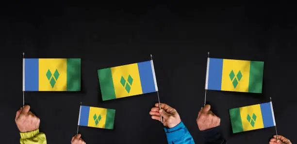 Hands holds flags of Saint Vincent and the Grenadines on dark background