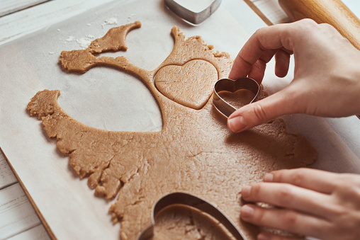 Making gingerbread cookies in shape of a heart for Valentines Day. Woman hand use cookie cutter. Holiday food concept