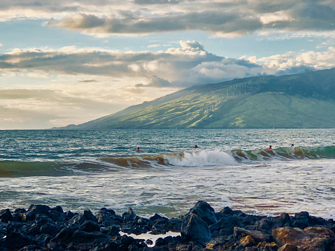 Maui, Hawaii USA 10/05/2018: Coastline along Kihei's Kamaole Beach Park III. The West Maui Mountains can be seen beyond swimmers playing in the surf.