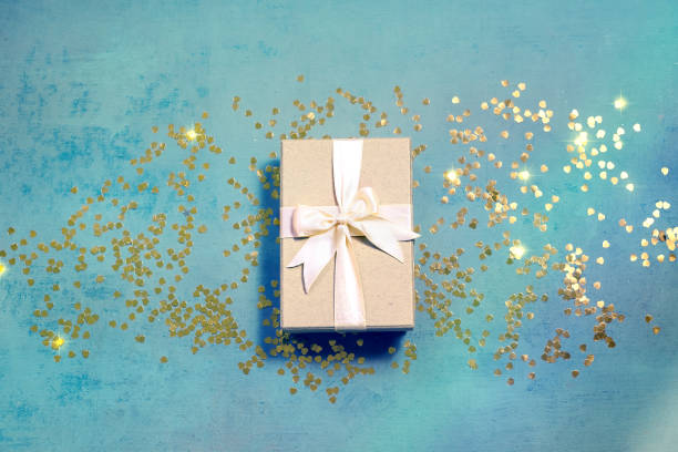 istock Present box with red bow on pastel blue background with golden confetti Flat lay 1197001372
