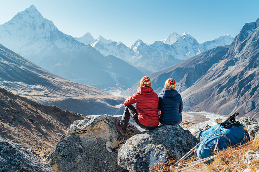 Pareja descansando en la ruta de senderismo Everest Base Camp cerca de Dughla 4620m. Los mochileros dejaron mochilas y bastones de trekking y disfrutan dotadas de vistas al valle con el pico Ama Dablam 6812m y Tobuche 6495m photo