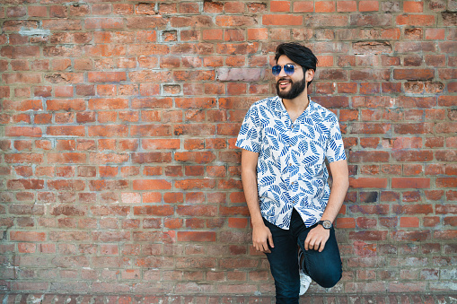 Portrait of young handsome man wearing summer clothes and sunglasses against brick wall. Urban concept.