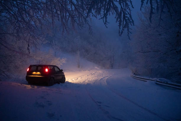 fahrer pov fahren auf schneebedeckter straße in der nacht, ersten schnee fallen. straße beleuchtet durch die scheinwerfer und die ampeln des vorderen autos. - drivers point of view country road snowing blizzard stock-fotos und bilder