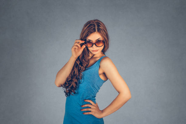 Headshot serious angry bitchy woman wife holding sunglasses down skeptically looking at you isolated gray wall background, blue shirt. Human face expression body language, attitude, perception