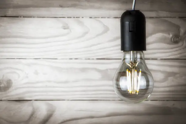 Photo of LED light bulb glowing on wooden background closeup.