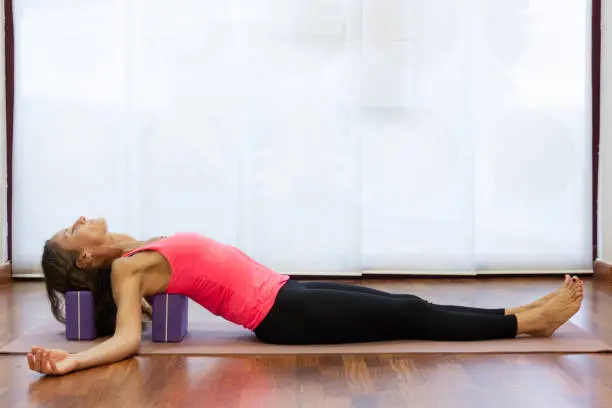 Photo of Slim woman rests back and head on blocks at yoga studio
