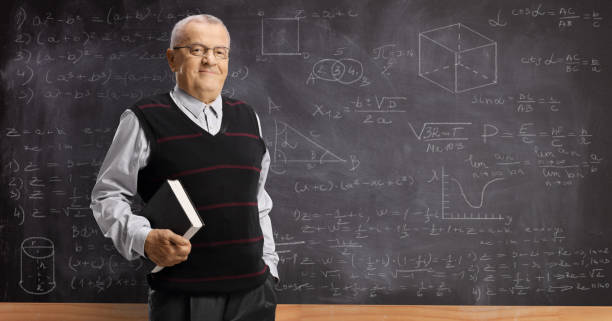 istock Elderly professor with a book standing in front of a blackboard 1197028315