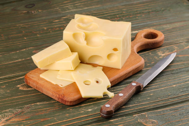 gelber käse mit löchern auf einem schneidebrett. - maasdam stock-fotos und bilder