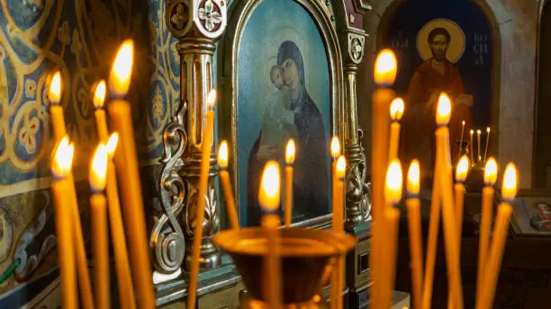 Photo of Blurred wax burning candles in an orthodox church on the icon background.