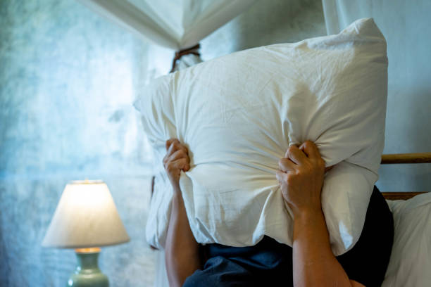 攻撃的な女性は枕と悲鳴で顔を覆った。 - oversleep ストックフォトと画像