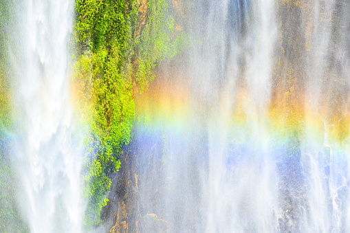 Close-up view of the Tumpak Sewu Waterfalls also known as Coban Sewu with a beautiful rainbow formed by refraction of light in water droplets. East Java, Indonesia.