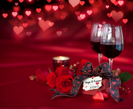 Valentine's Day Red Roses and Red Wine with a Gift on a Defocused Lights Background