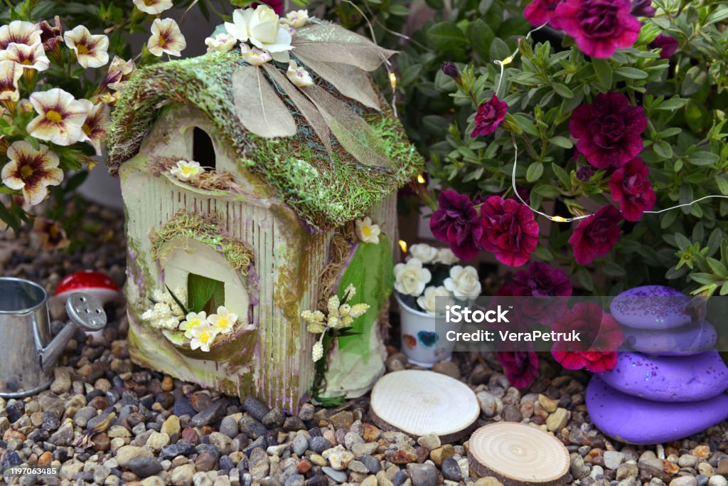 Small fairy cottage with petunia flowers outside in the garden. Small fairy cottage with petunia flowers outside in the garden. Lovely miniature house for greeting cards, wedding or birthday concept. Vintage summer background Fairy Stock Photo