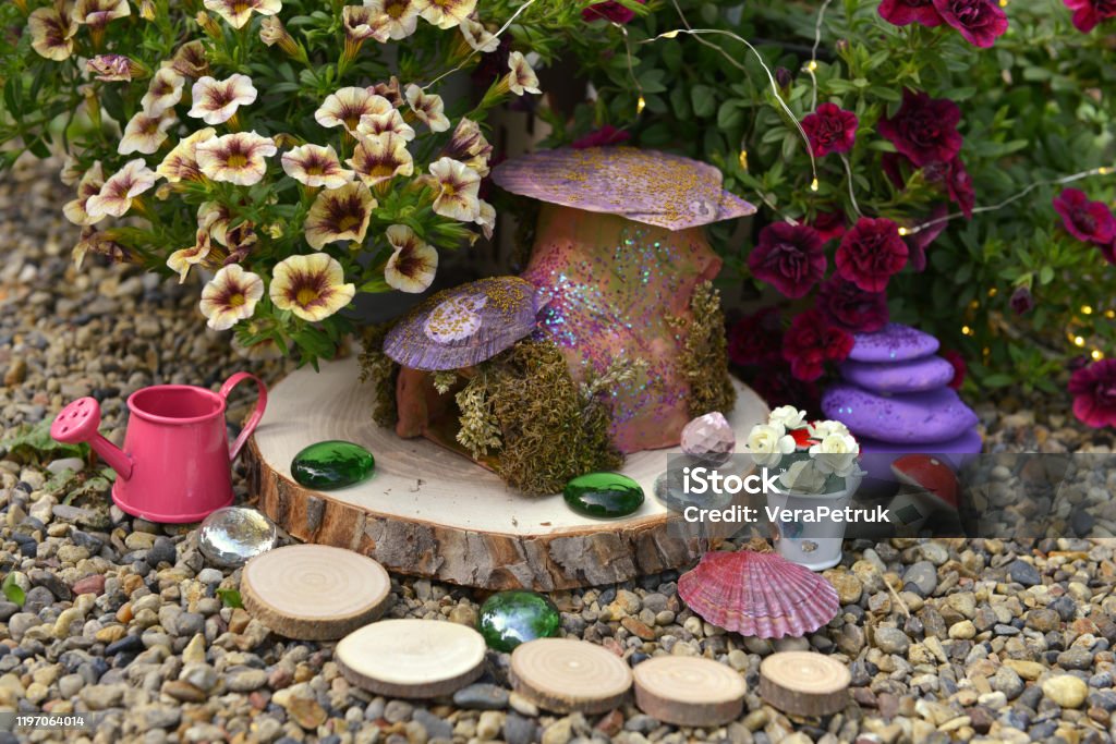 Funny fairy dollhouse on wooden planks by flowerbed with petunia flowers in the garden. Lovely miniature house for greeting cards, wedding or birthday concept. Vintage summer background Funny fairy dollhouse on wooden planks by flowerbed with petunia flowers in the garden. Fairy Stock Photo