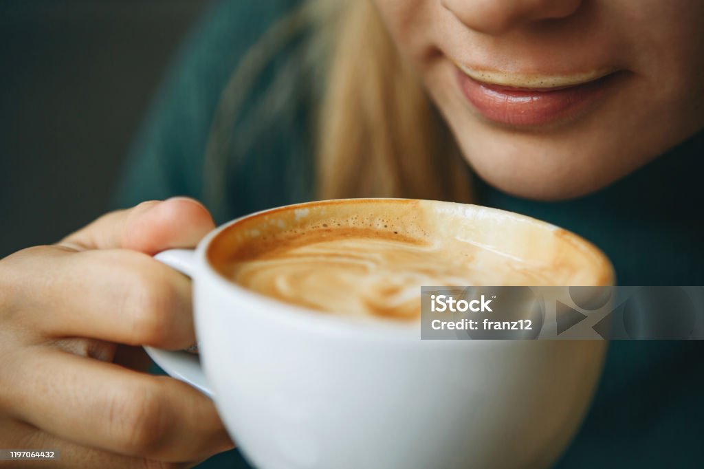 Close up girl is drinking coffee Close up girl is drinking coffee. She has coffee foam on her lips and she smiles. She is enjoying her morning cappuccino. Coffee - Drink Stock Photo