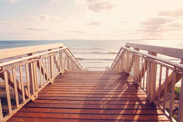 Timber stairs with safety railings leading down to the beach, with sand and surf at the bottom, all bathed in early morning light shining across the ocean