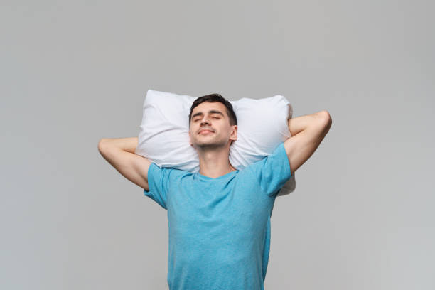 istock Tired brunet man in a blue tee resting on a white pillow isolated over grey background. 1197069643