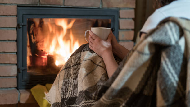 격자 무늬로 덮인 젊은 성인 여성의 자른 전망은 편안한 집에서 벽난로와 유리 문 근처에 앉아있습니다. 소녀 앉아 에 홈 와 컵 의 음료 - blanket fireplace winter women 뉴스 사진 이미지