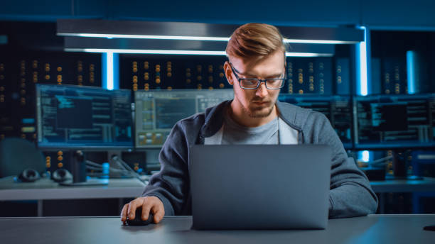 istock Portrait of Software Developer / Hacker Wearing Glasses Sitting at His Desk and Working on Computer in Digital Identity Cyber Security Data Center. Hacking or Programming. 1197071000