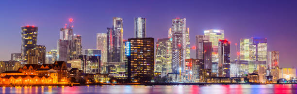 Panoramic View of the Canary Wharf London City Skyline at Sunset and River Thames, England Illuminated Buildings at Twilight with Clear Sky clear sky night sunset riverbank stock pictures, royalty-free photos & images