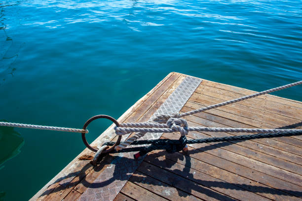A thick metal chain is firmly attached to a dock, resting on a sturdy surface, with rippling water seen in the background under clear, sunny skies.