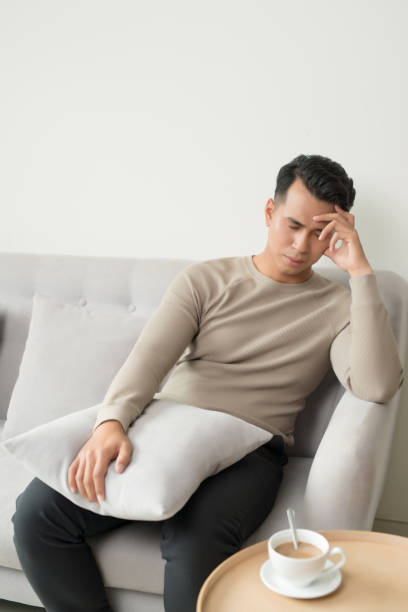 istock Young man suffering from headache after hard working day, sitting on couch at home, copy space 1197076536