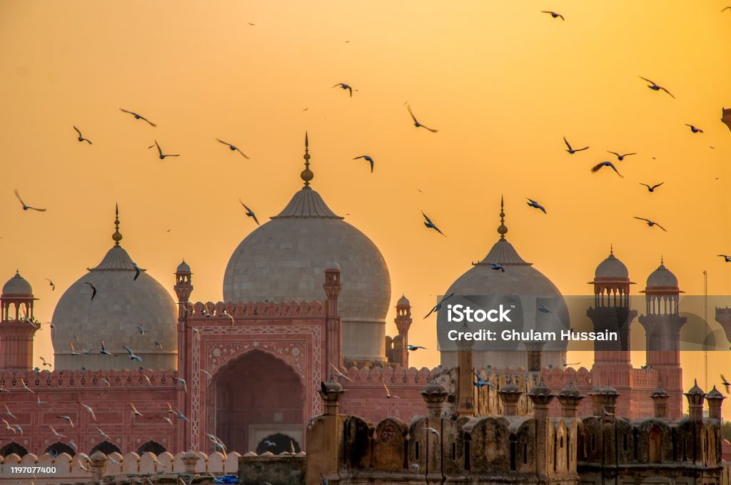 Flying birds over the mosque Fascinating view of Badshahi mosque during sunset. This is biggest mosque in the world Pakistan Stock Photo