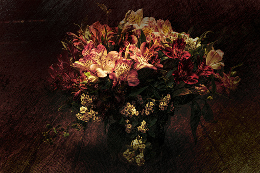 A beautifully put together bouquet of flowers on an old wooden table. Incalilia shine in the middle in beautiful colors and stand out from the dark background of the wooden structure of the table.
