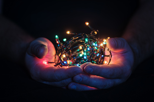 male hands holding a Christmas garland with lights on a dark background with copy space for text. Retro effect, close-up. Winter, postcard template