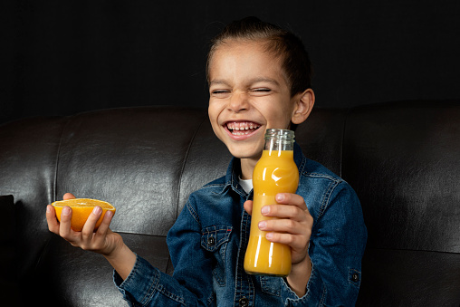 little boy is holding fresh orange and drinking fresh juice on black background