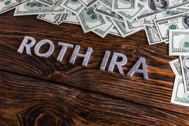 Photo of words ROTH IRA laid on wooden surface with metal letters and us dollar banknotes