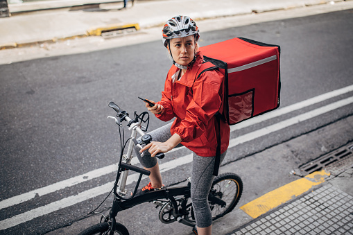 Bicycle delivery woman with road bicycle in the city checking delivery address on mobile app