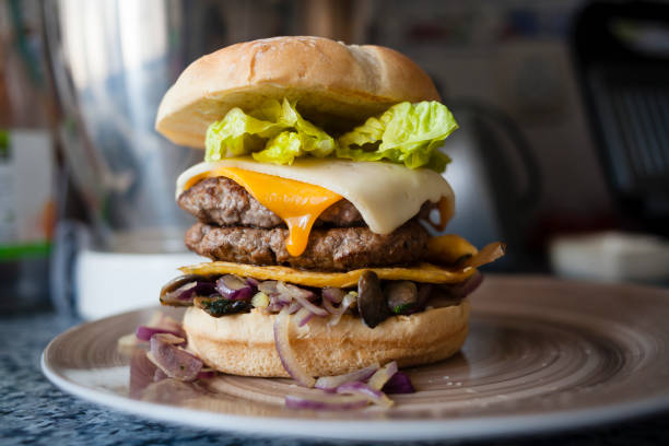 Food styling shot of a plated delicious fresh made burger sandwich made with artisan bread, double beef meat, havarti and cheddar melted cheese, purple onion, egg omelet, mayo sauce and lettuce.