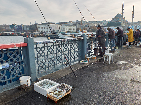 İstanbul, Turkey - April 12, 2006: People trying to fish with line fishing on the Bosphorus shore in Sariyer - Bosphorus Bridge is seen in the background.